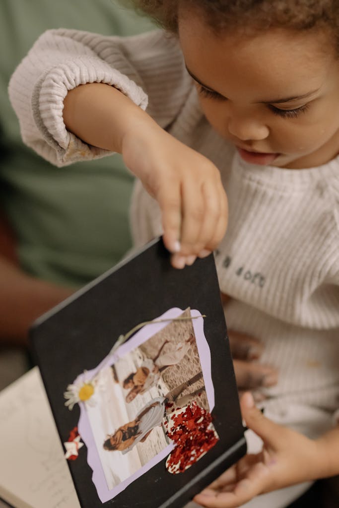 A young child curiously examines a family photo album indoors, depicting a moment of exploration and nostalgia.